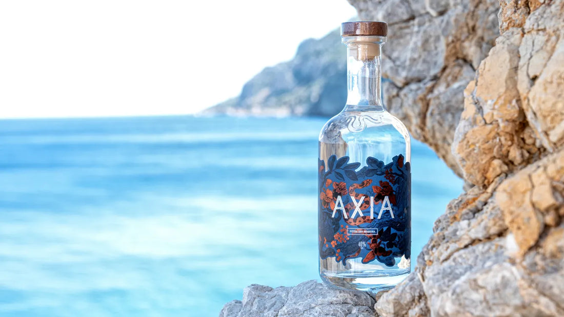 Bottle of Axia Mastiha greek spirit against a scenic coastal background with blue water and rocky cliffs in Greece