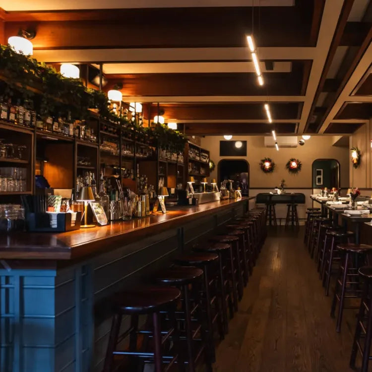 Avoca, New York: warmly lit, traditional-style bar with a long wooden countertop, dark stools, and shelves stocked with bottles and glasses