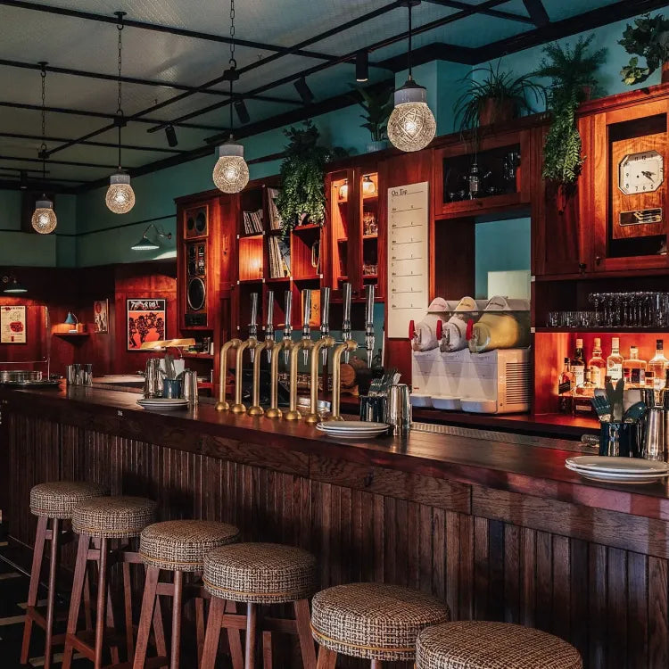 Dishoom Permit Room, Brighton: classic pub interior with a wooden bar, stools, beer taps, and hanging pendant lights