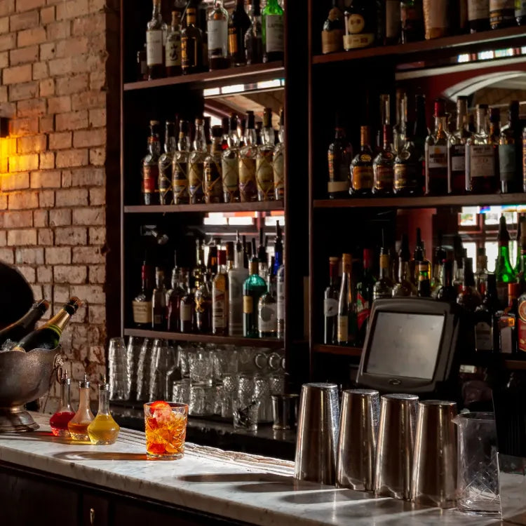 Experimental Cocktail Club Soho, London: warmly lit bar with shelves packed with liquor bottles, cocktail shakers, and a cocktail drink on the counter