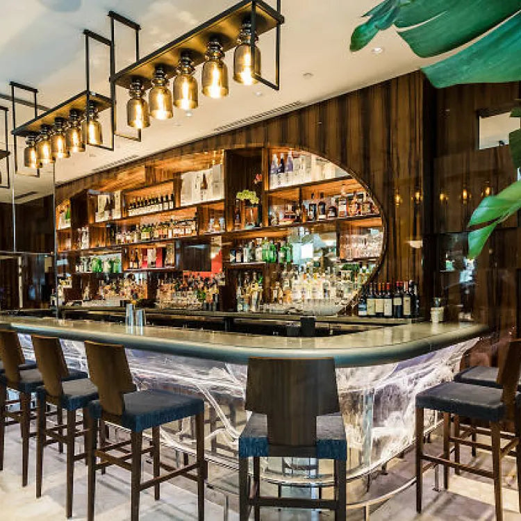 Novikov, Miami: well-lit bar area with a modern design, featuring a long counter with stools, a fully stocked back bar, and unique hanging light fixtures