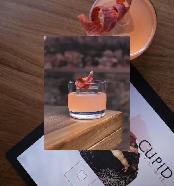 Axia Mastiha Spirit with A for Athens Cupid Cocktail on a wooden table with a secondary picture in the background of another Axia Mastiha Spirit and A for Athens cocktail