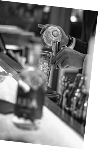 Black and white picture of barman making Axia Spirit Classic Cocktail next to a bottle at a bar