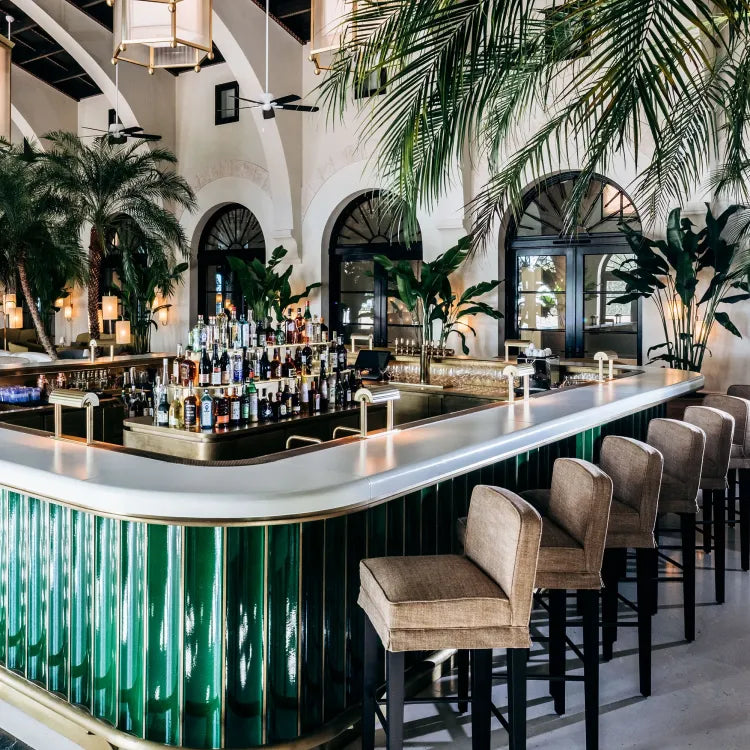 Four Seasons Surfside, Miami: stylish, brightly lit bar with green and gold counter, several brown velvet bar stools and lush tropical plants and palm trees decorating the surrounding area