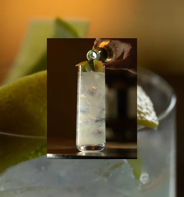 Axia Mastiha Greek Spirit and Oriole London Axia Lemonade Cocktail being made on a bar with secondary blurred picture in the background of another Axia Lemonade Cocktail