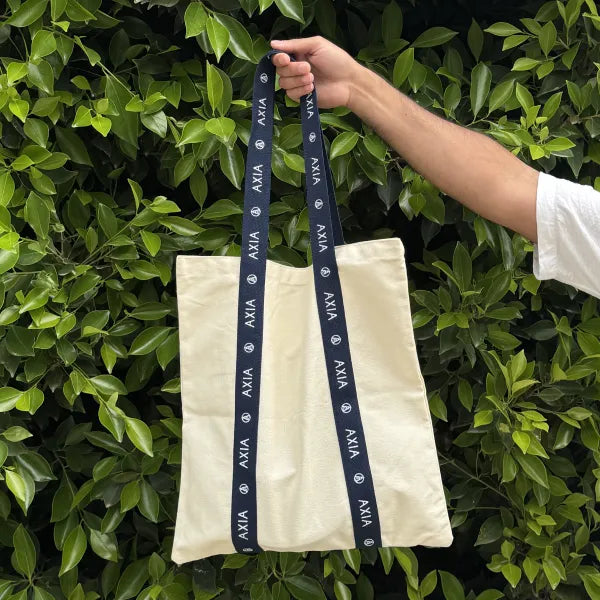 Axia Spirit Cotton Tote Bag held by someone in front of a lush green foliage