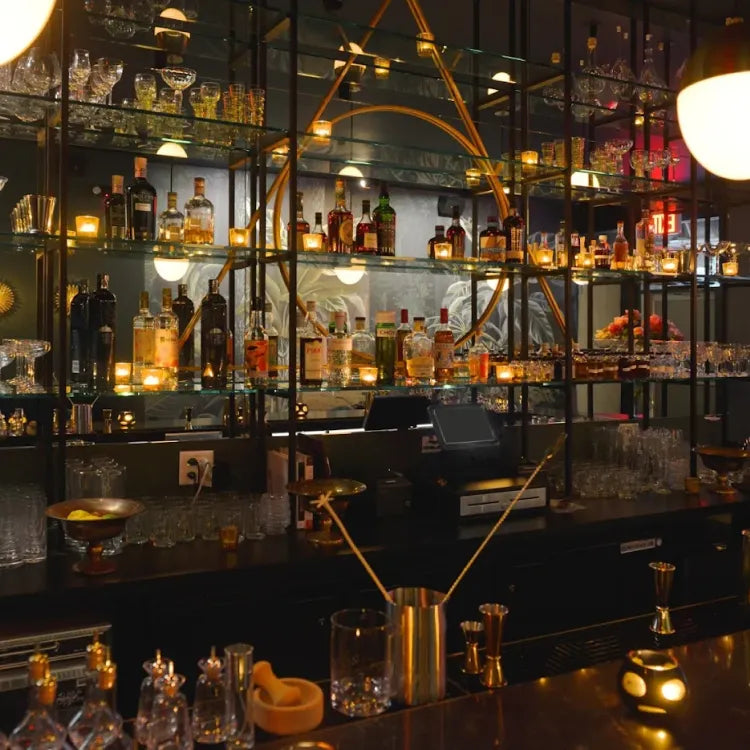 Sugar Monk, New York: dimly lit, sophisticated bar with a dark countertop and shelves stocked with various bottles and glassware, illuminated by warm accent lighting