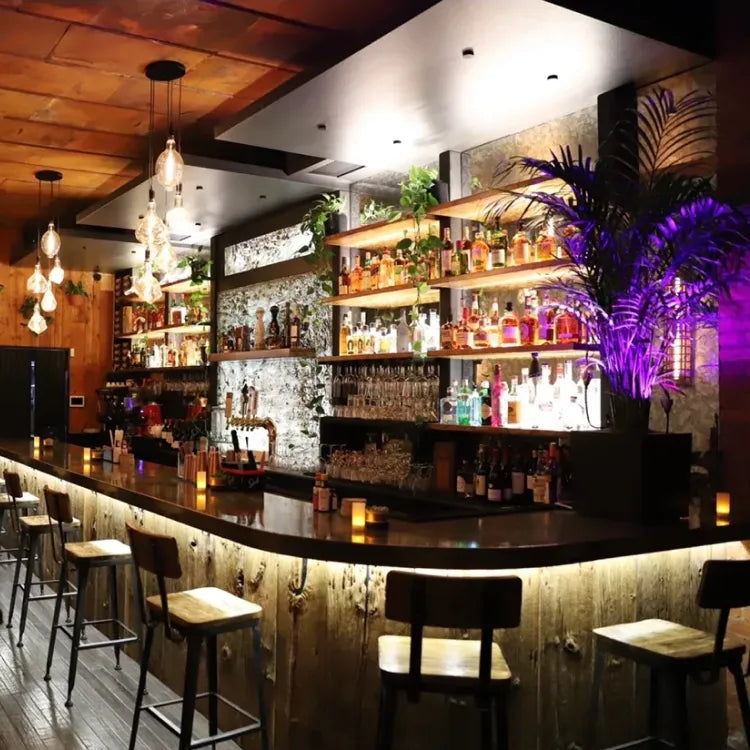 The Rusty Face, New York: warmly lit bar area with a curved dark countertop, wooden bar stools, and shelves stocked with bottles and glasses