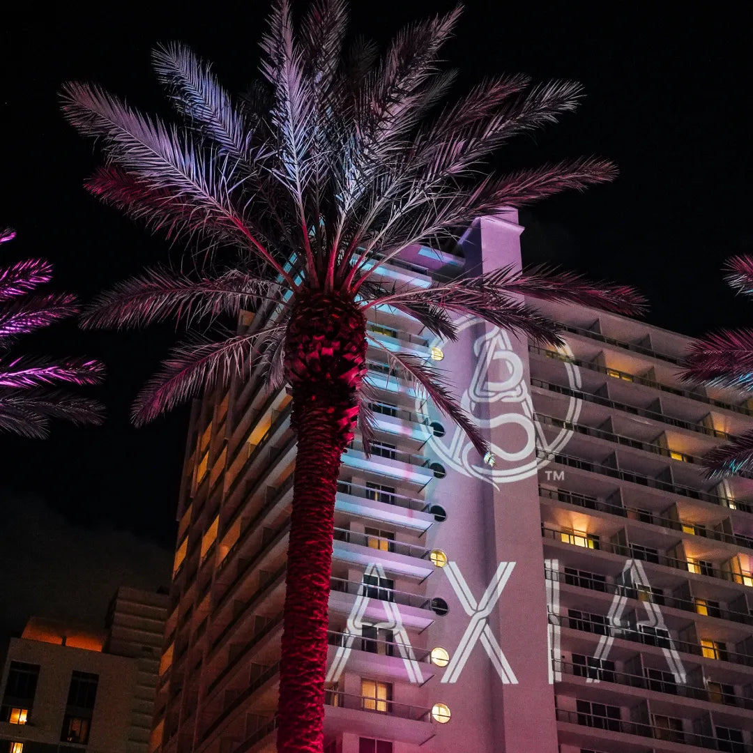 Axia logo being projected on a building at night with light and a palm tree at the front