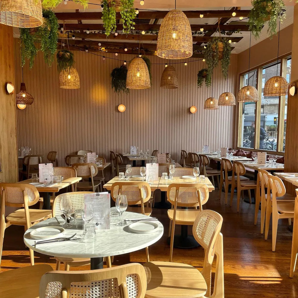 Brother Marcus, UK: Cosy restaurant interior with wooden furniture, wicker light fixtures, and green plants.