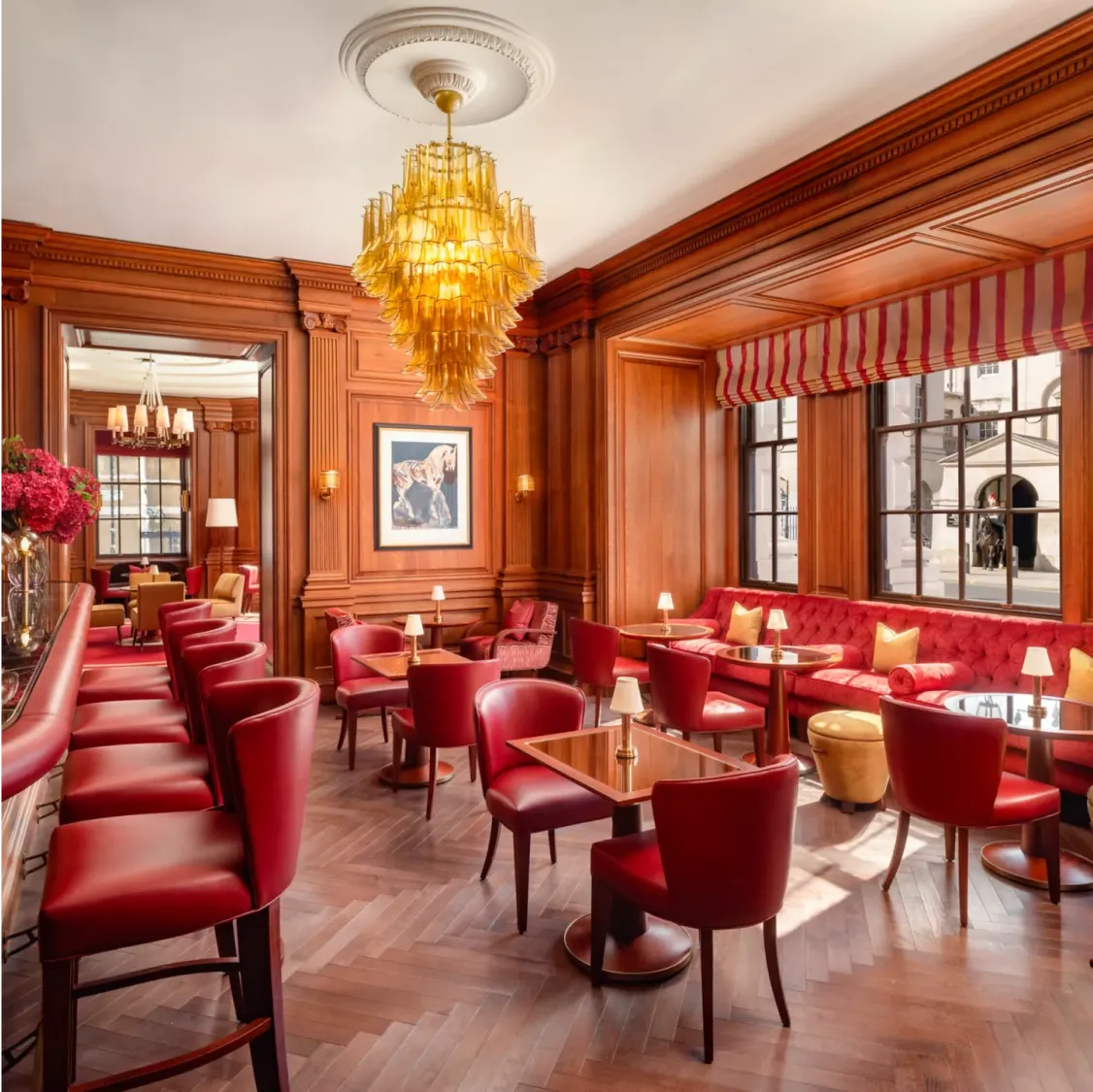 Raffles, London: Elegant bar with red chairs, wooden walls, and a chandelier.
