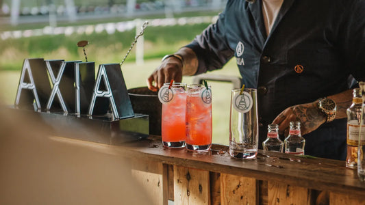 Axia mastiha Greek spirit cocktails being served at an outdoor bar with London Essence, with branded glassware and signage during a summer event