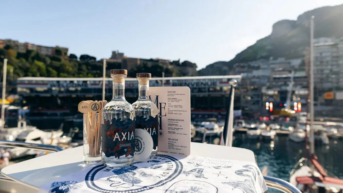 Two Axia Mastiha Greek spirit bottles next to an Axia menu, cocktail sticks and tea towel on a table near yachts