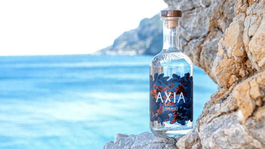 Bottle of Axia Mastiha greek spirit against a scenic coastal background with blue water and rocky cliffs in Greece