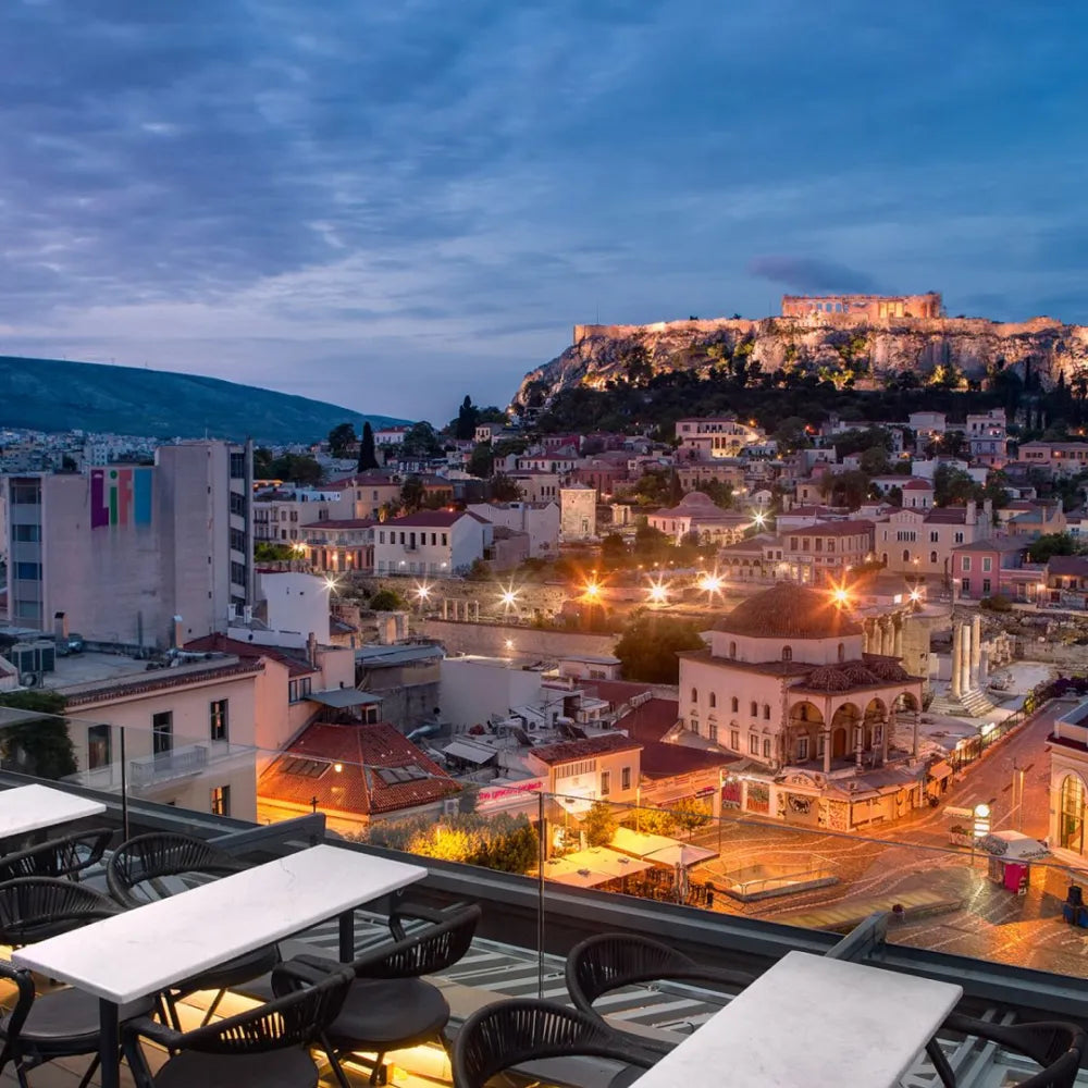 A for Athens Bar Restaurant: Rooftop view of Athens at dusk, featuring illuminated Acropolis and surrounding buildings.