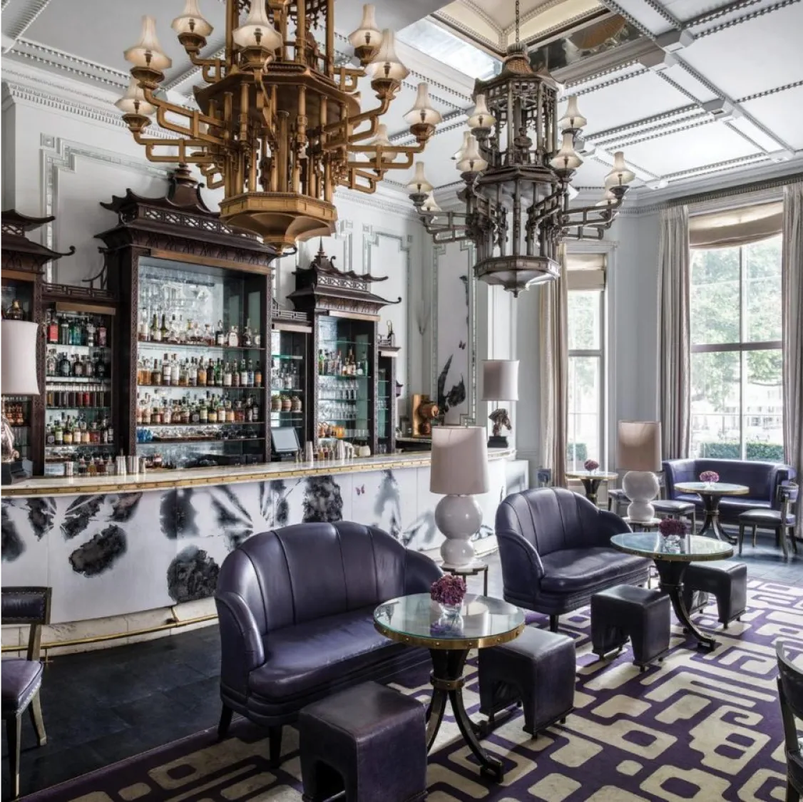 Artesian at The Langham, London: Elegant bar with chandeliers, purple seating, and a well-stocked counter.