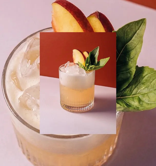 Axia Greek Mastiha Spirit Basilisk Smash Cocktail with ice, peach slices and basil on a red background with a secondary picture in the background of another Basilisk Smash cocktail