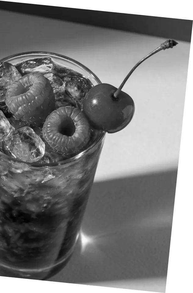 Black and white picture of an Axia Greek Mastiha Spirit Bramble Cocktail with ice, raspberries, and a cherry