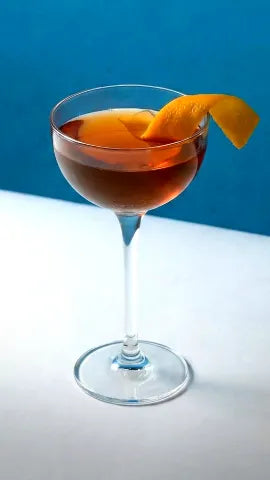 Axia Greek Mastiha Spirit Classic Cocktail with orange peel on a blue background