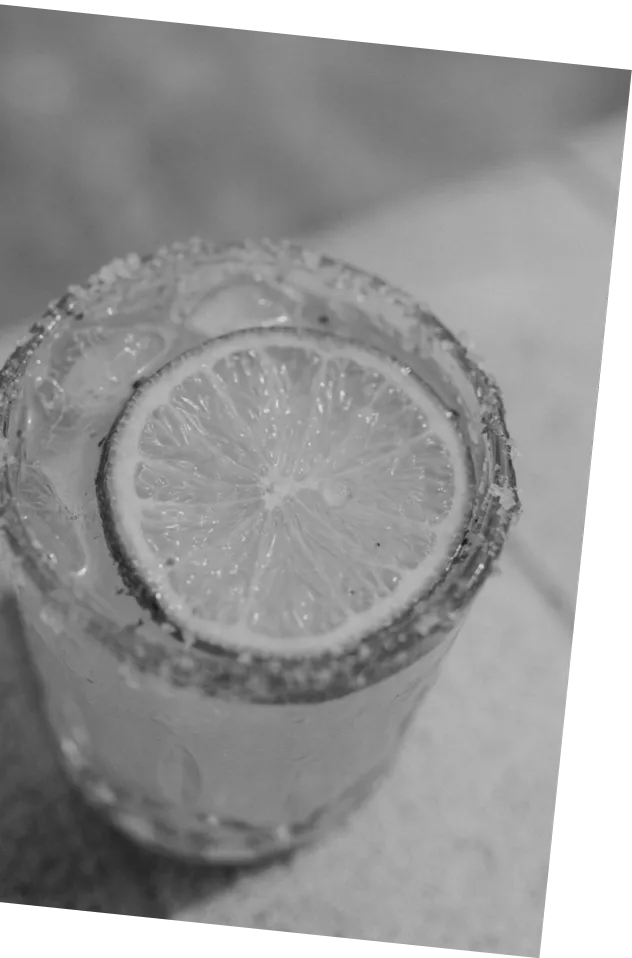 Black and white picture of an Axia Greek Mastiha Spirit Margarita Cocktail with a lime wedge, ice cubes and salt next to a swimming pool