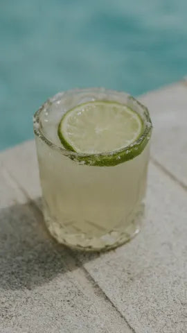 Axia Greek Mastiha Spirit Margarita Cocktail with a lime wedge, ice cubes and salt next to a swimming pool