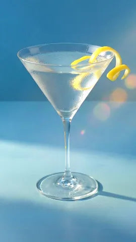 Axia Greek Mastiha Spirit Martini Cocktail with lemon peel on a light blue background