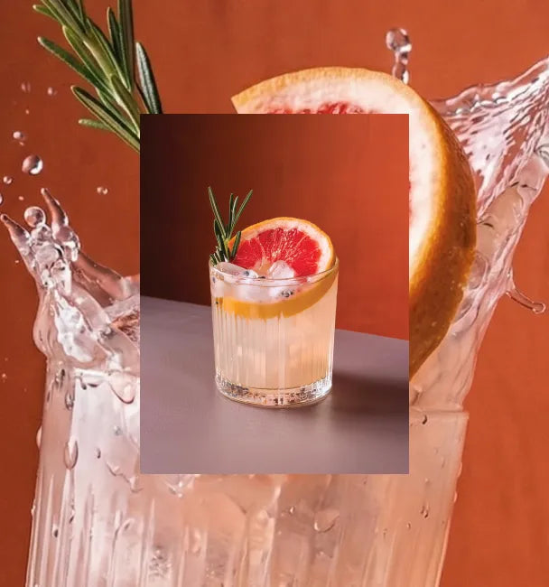 Axia Greek Mastiha Spirit Aegean Paloma Cocktail with grapefruit slice and rosemary garnish on a gradient orange background with a secondary picture in the background of another Paloma cocktail