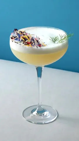Axia Greek Mastiha Spirit Sour Japanese Cocktail with flowers and dill on a blue background