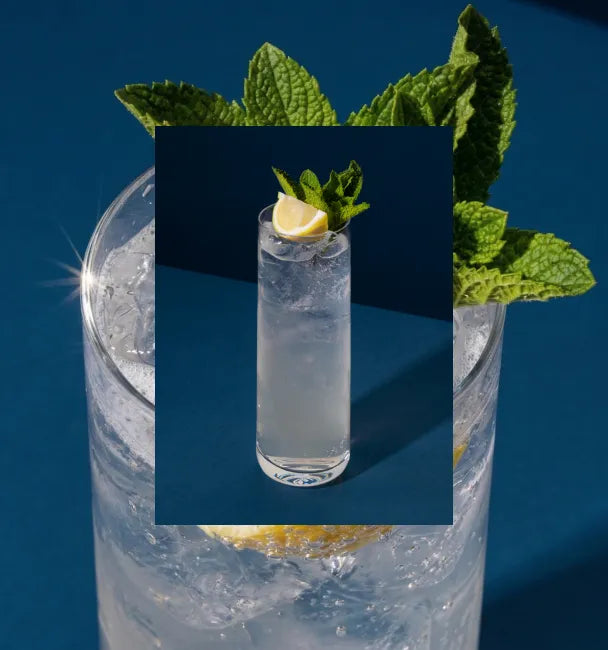 Axia Greek Mastiha Spirit Twisted Lemon Cocktail with ice, lemon and mint leaves on a blue background with a secondary picture in the background of another Twisted Lemon cocktail