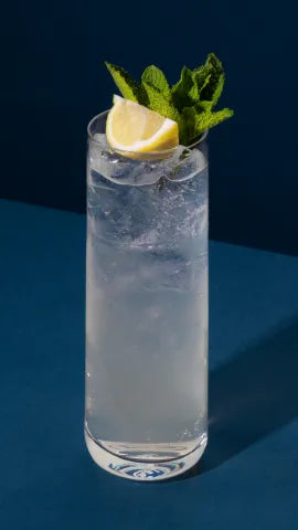 Axia Greek Mastiha Spirit Twisted Lemon Cocktail with ice, lemon and mint leaves on a blue background