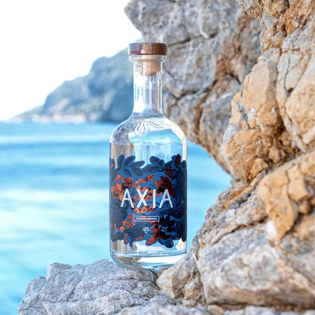 Bottle of Axia Mastiha greek spirit against a scenic coastal background with blue water and rocky cliffs in Greece