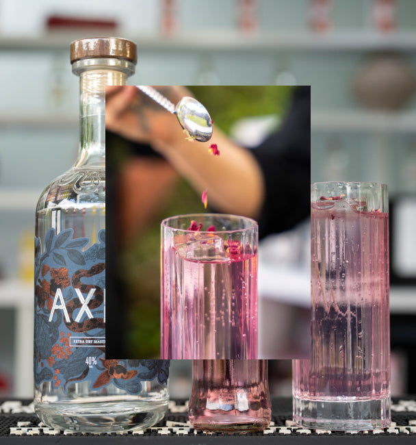 Axia Mastiha Spirit and London Essence Raspberry and Rose Soda with rose water and petals cocktail with a secondary picture in the background of another Axia and London Essence cocktail next to an Axia Extra Dry Mastiha Spirit bottle on a bar