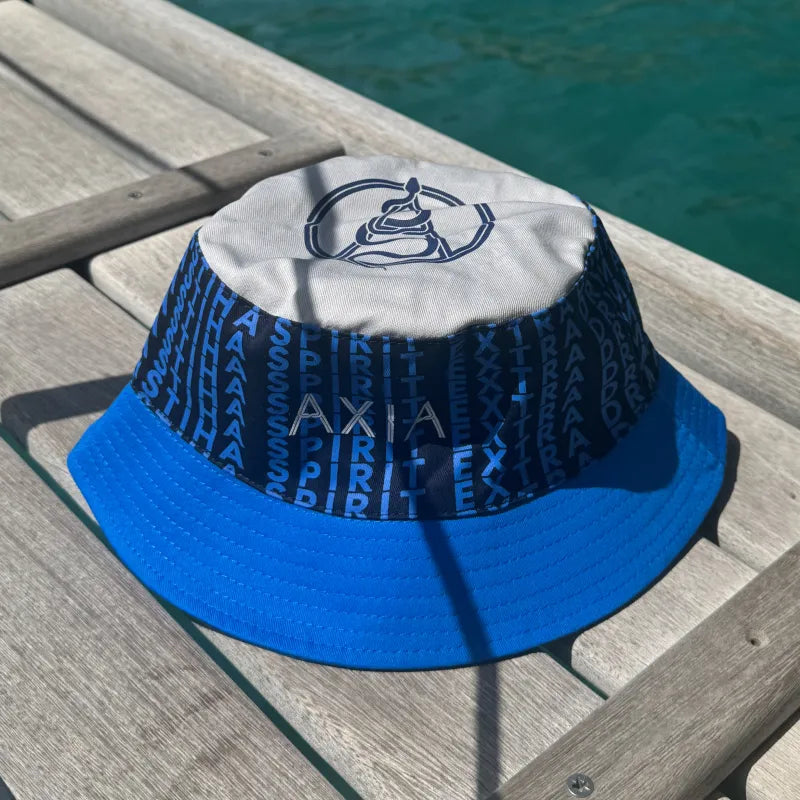 Axia Bucket Hat in different shades of Axia blue and written Extra Dry Mastiha Spirit on it multiple times on a wooden dock by the sea