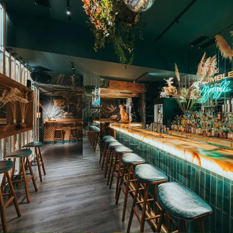 The bar in front of the bar, Athens: Bar interior with green tiled bar and wooden stools in a stylish setting.