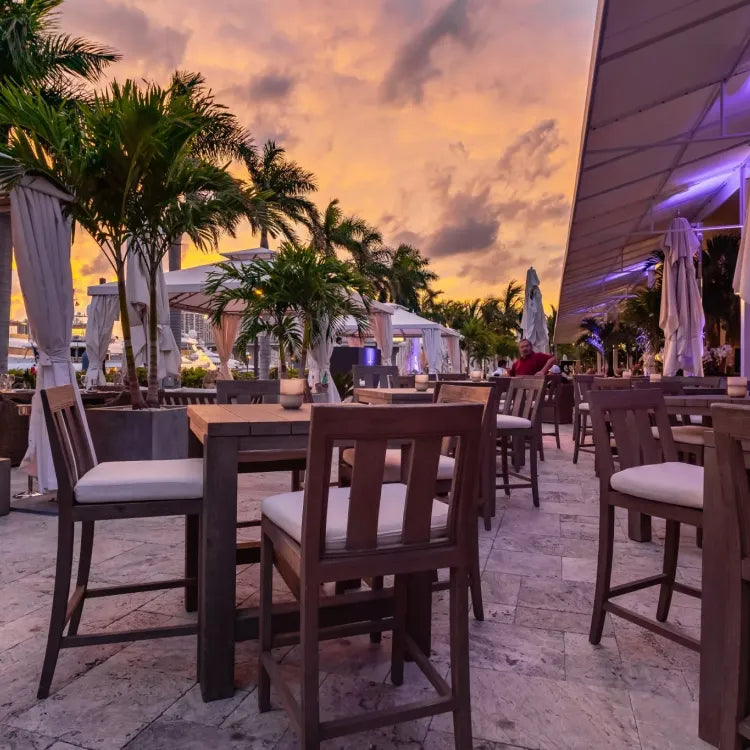 The Deck at Island Gardens, Miami: outdoor restaurant seating area at dusk with palm trees and a colorful sky