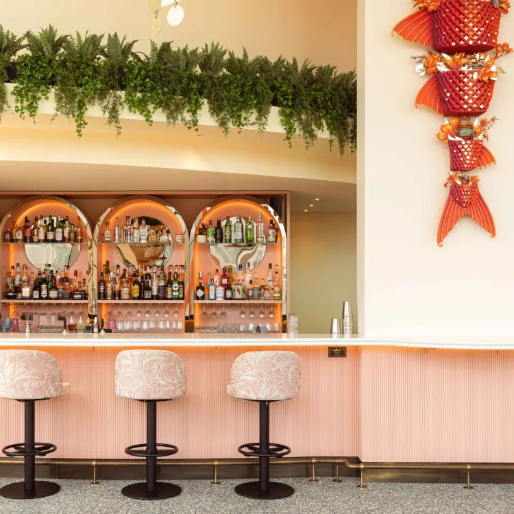 Joia Battersea, London: Glamorous bar with pink stools, green plants, and decorative wall art.