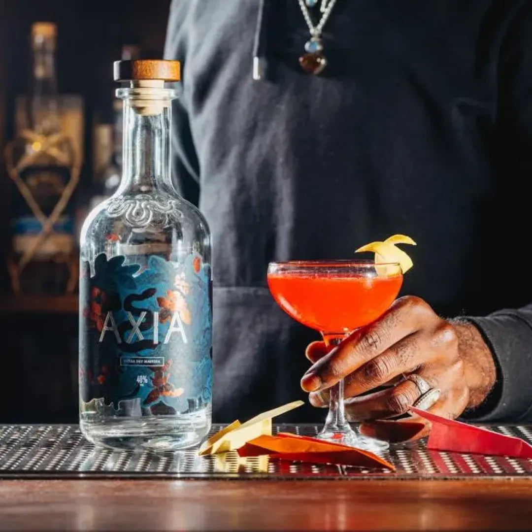 Bottle of Axia Spirit on a bar next to a hand holding a cocktail glass